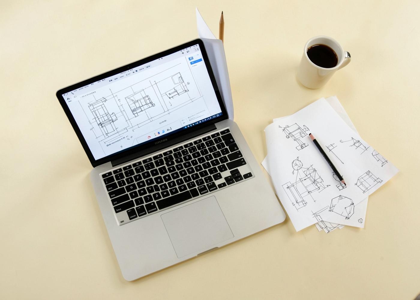 Overhead view of a workspace with a laptop showing wireframe sketches, printed diagrams, a pencil and a cup of coffee